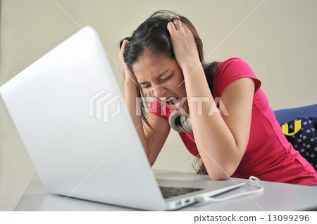A young Asian female student feeling stressed over her school work / reseach in front of laptop 13099296