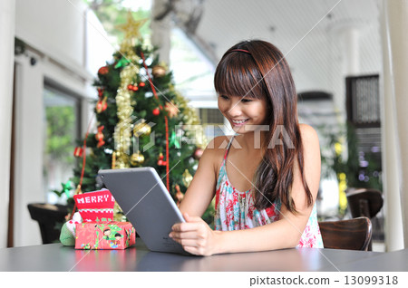 A young and beautiful Asian lady using her tablet while waiting for her friends to celebrate Xmas 13099318
