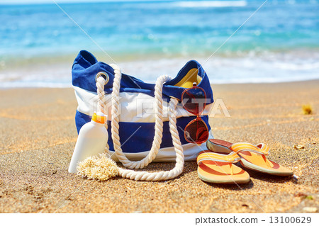 Beach bag, flip flops and sunscreen on beach 13100629