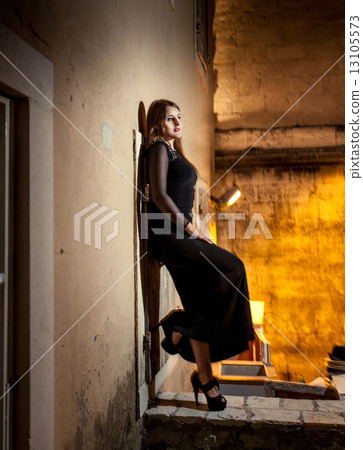 woman in long dress leaning against wall on old street at night 13105573