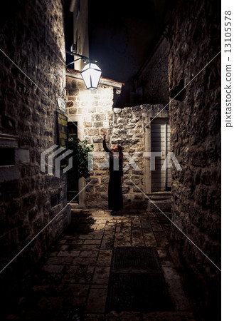 woman walking on narrow street lit by gas lantern 13105578