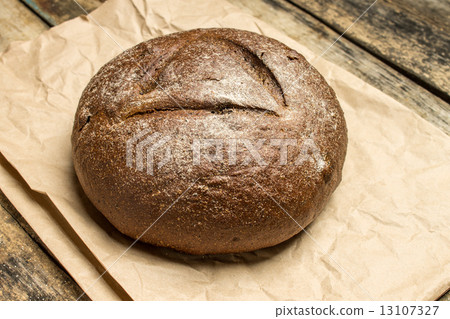 Fresh baked loaf of bread on paper bag at wooden table 13107327