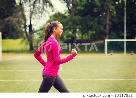smiling young woman running on track outdoors 13117858