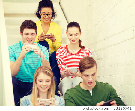 smiling students with smartphone texting at school smiling students with smartphone texting at school 13120741