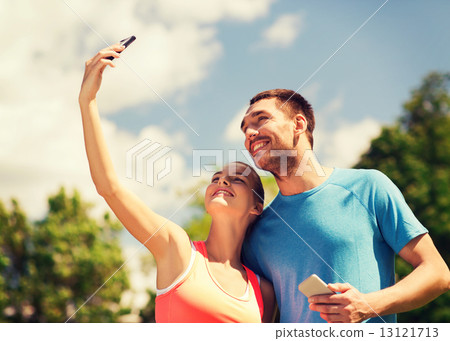 two smiling people with smartphones outdoors 13121713
