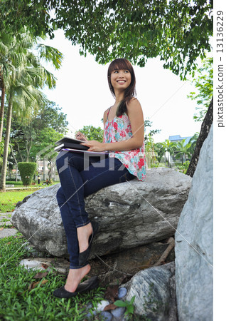 A portrait of young and beautiful Asian lady using her tablet relaxing in the garden  13136229
