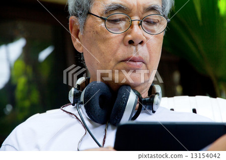 Senior man sitting outside reading E-book on his tablet.  13154042