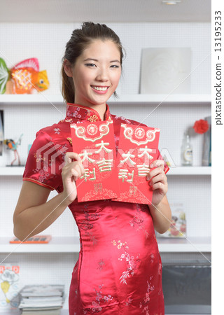 One young Chinese woman in cheogsam holding 2 big red packet in front of bookshelf One young Chinese woman in cheogsam holding 2 big red packet in front of bookshelf 13195233