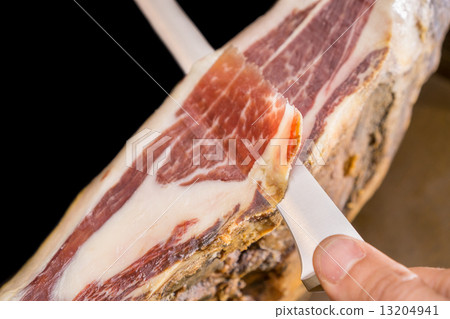 Top view of knife and hand cutting Serrano ham, black background 13204941