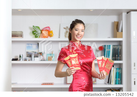 Young Chinese woman in cheongsam holding 5 red packets in a fan shape in front of bookshelf 13205542