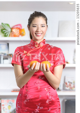 Young chinese woman in cheongsam holding oranges in front of bookshelf 13205635