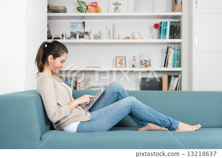 One young chinese woman using mobile device tablet iPad relaxing on a sofa 13218637