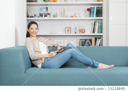 One young chinese woman using mobile device tablet iPad relaxing on a sofa 13218640
