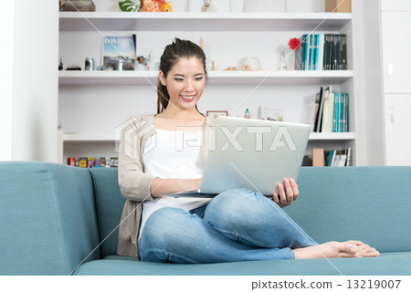 One young chinese woman using mobile device laptop relaxing on a sofa 13219007