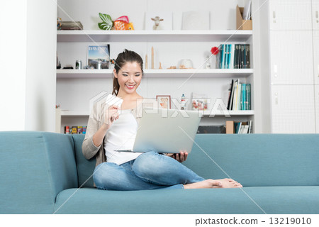 One young chinese woman shopping online using laptop and credit card while relaxing at home 13219010