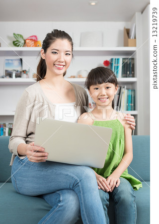 Young chinese mother and daughter using mobile device laptop at home 13219739