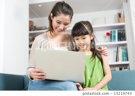 Young chinese mother and daughter using mobile device laptop at home 13219743