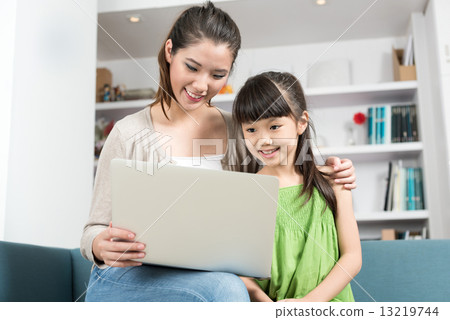 Young chinese mother and daughter using mobile device laptop at home 13219744