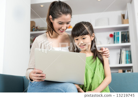 Young chinese mother and daughter using mobile device laptop at home 13219745