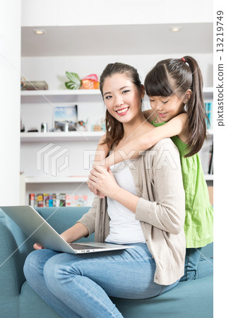 Young chinese daughter hugging mother while she is using mobile device laptop at home 13219749