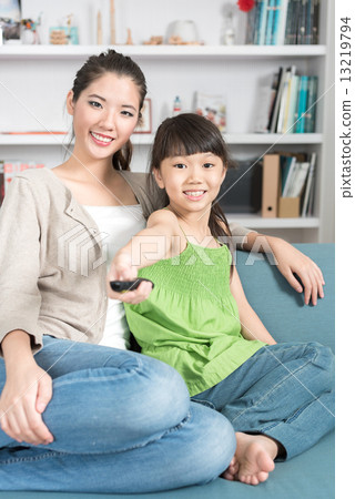 Young chinese daughter changing TV channel while watching with mother at home 13219794