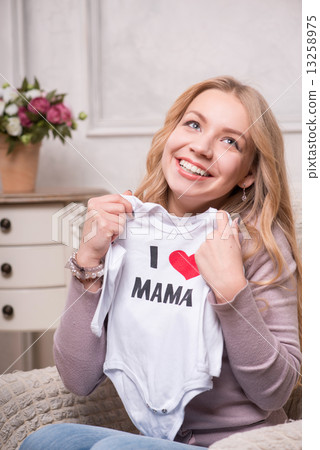 Young attractive woman holding white baby bodysuit, interior sho Young attractive woman holding white baby bodysuit, interior sho 13258975