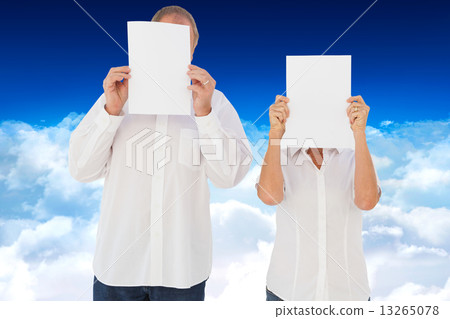 Composite image of couple holding paper over their faces Composite image of couple holding paper over their faces 13265078