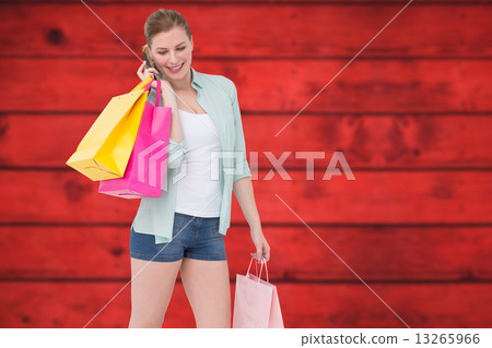Composite image of happy blonde holding shopping bags and talkin 13265966