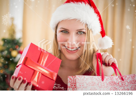Composite image of festive blonde showing a gift while looking a Composite image of festive blonde showing a gift while looking a 13266196