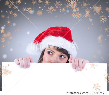 Composite image of festive brunette holding a poster while looki Composite image of festive brunette holding a poster while looki 13267475