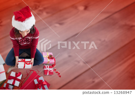 Composite image of festive brunette sitting and wrapping christm 13268947