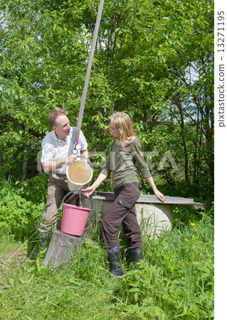 Young happy pair at a well, pours water in a bucket 13271195