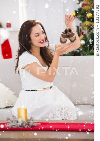 Composite image of happy brunette holding baby shoes at christmas Composite image of happy brunette holding baby shoes at christmas 13277392