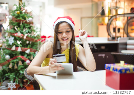 A beautiful and young Pan-Asian lady wearing a Santa hat doing online shopping using her credit card A beautiful and young Pan-Asian lady wearing a Santa hat doing online shopping using her credit card 13282797