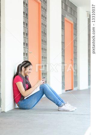 One young pan asian female student text messaging while studying along campus corridor 13310037