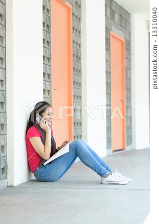One young pan asian female student making a call while studying along campus corridor One young pan asian female student making a call while studying along campus corridor 13310040