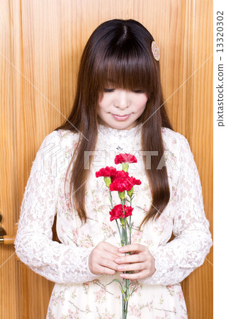 A woman with carnation flowers in front of a tree wall 13320302