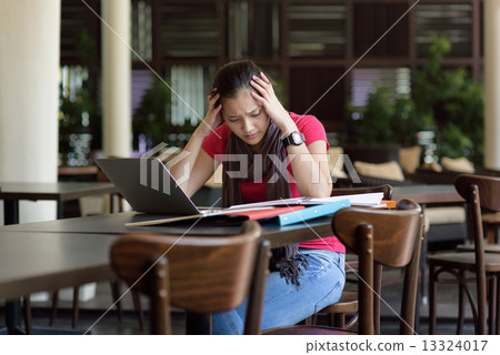 One young pan asian female student stressed over examination in campus cafe 13324017