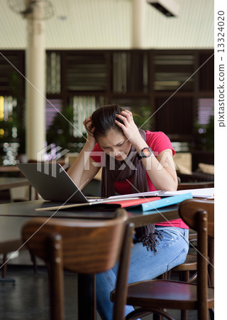 One young pan asian female student stressed over examination in campus cafe 13324020