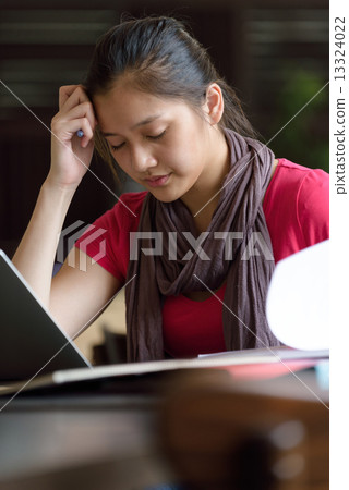 One young pan asian female student stressed over examination in campus cafe 13324022
