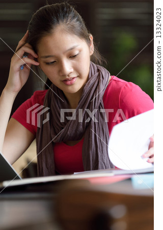 One young pan asian female student stressed over examination in campus cafe 13324023