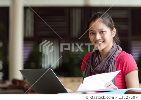 One young pan asian female student studying hard for examination in campus cafe 13327597