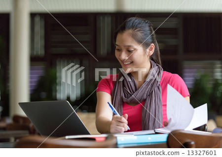 One young pan asian female student studying hard for examination in campus cafe 13327601