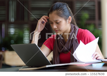 One young pan asian female student studying hard for examination in campus cafe 13327630
