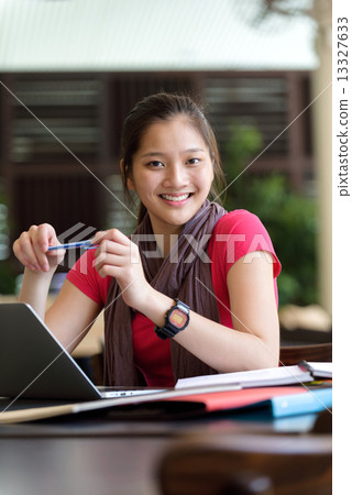One young pan asian female student studying hard for examination in campus cafe 13327633