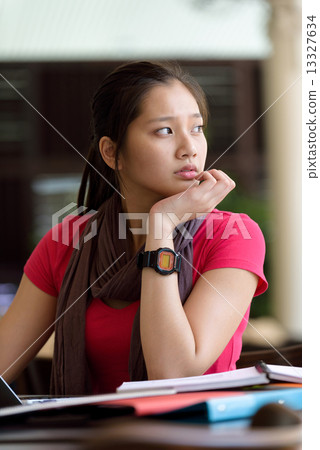 One young pan asian female student studying hard for examination in campus cafe 13327634