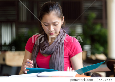 One young pan asian female student studying hard for examination in campus cafe 13327637