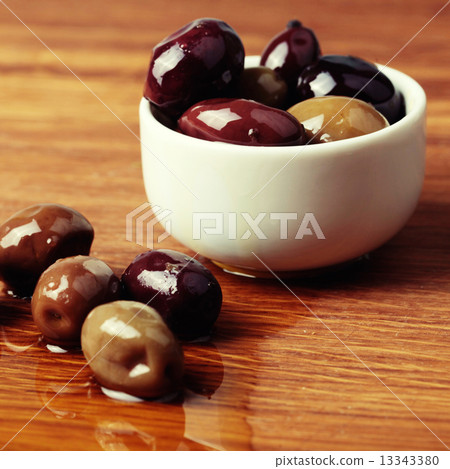 different olives in white bowl on wooden board 13343380