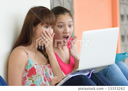 2 young female chinese student using laptop sitting along campus corridor 13353262