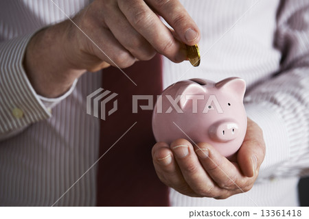 Businessman Putting Coin Into Piggy Bank 13361418